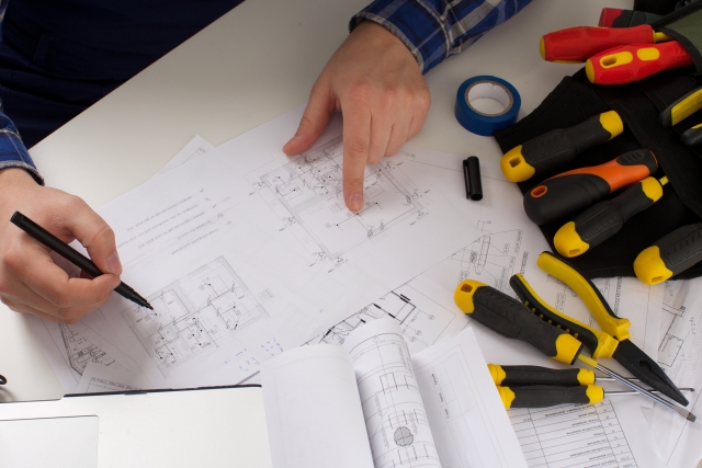 設計図を指差しながら工具を使って作業計画を立てる人