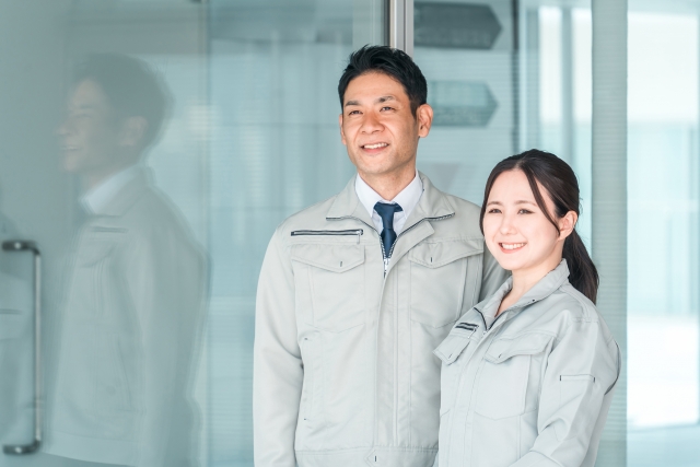 作業着を着た男女スタッフが並んで笑顔を見せている様子