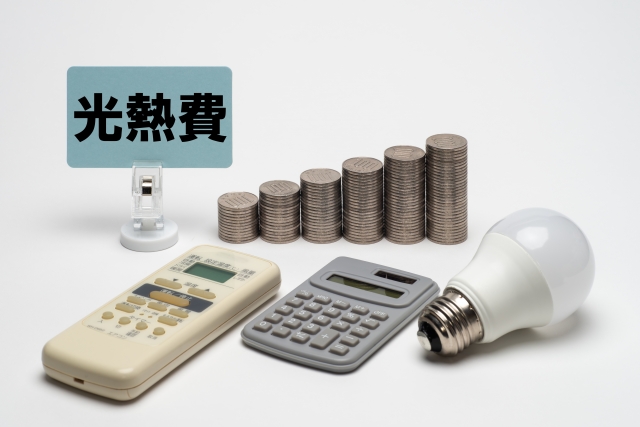 光熱費をイメージした電卓・リモコン・電球と積み重ねられた硬貨の写真